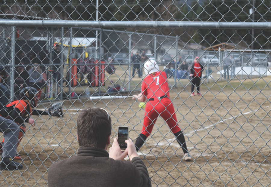 A+softball+player+swings+at+the+ball+at+a+softball+game+with+her+father+and+coach+watching+on.